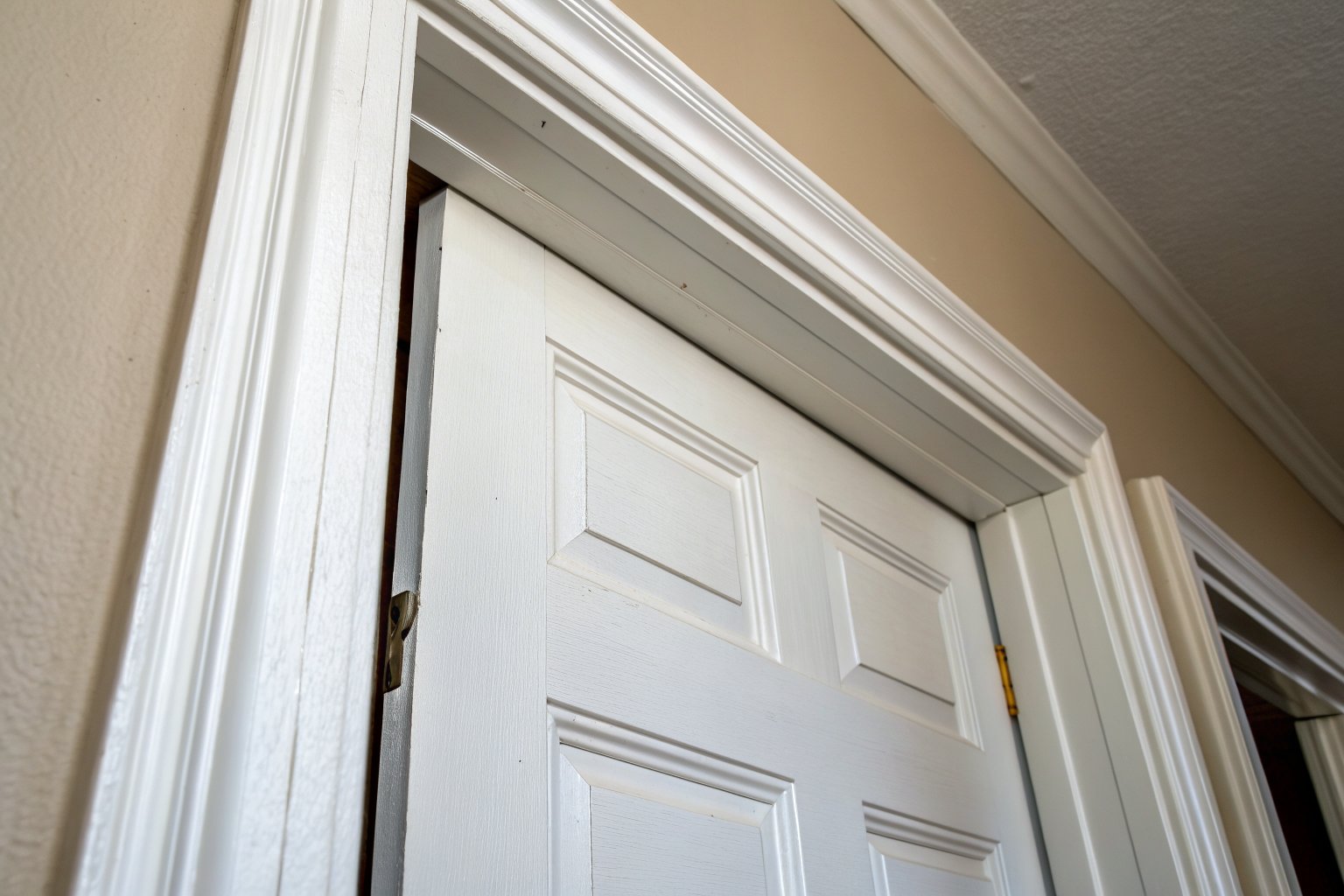 White six-panel interior door hanging crooked, with a dark gap along the hinge side of the frame