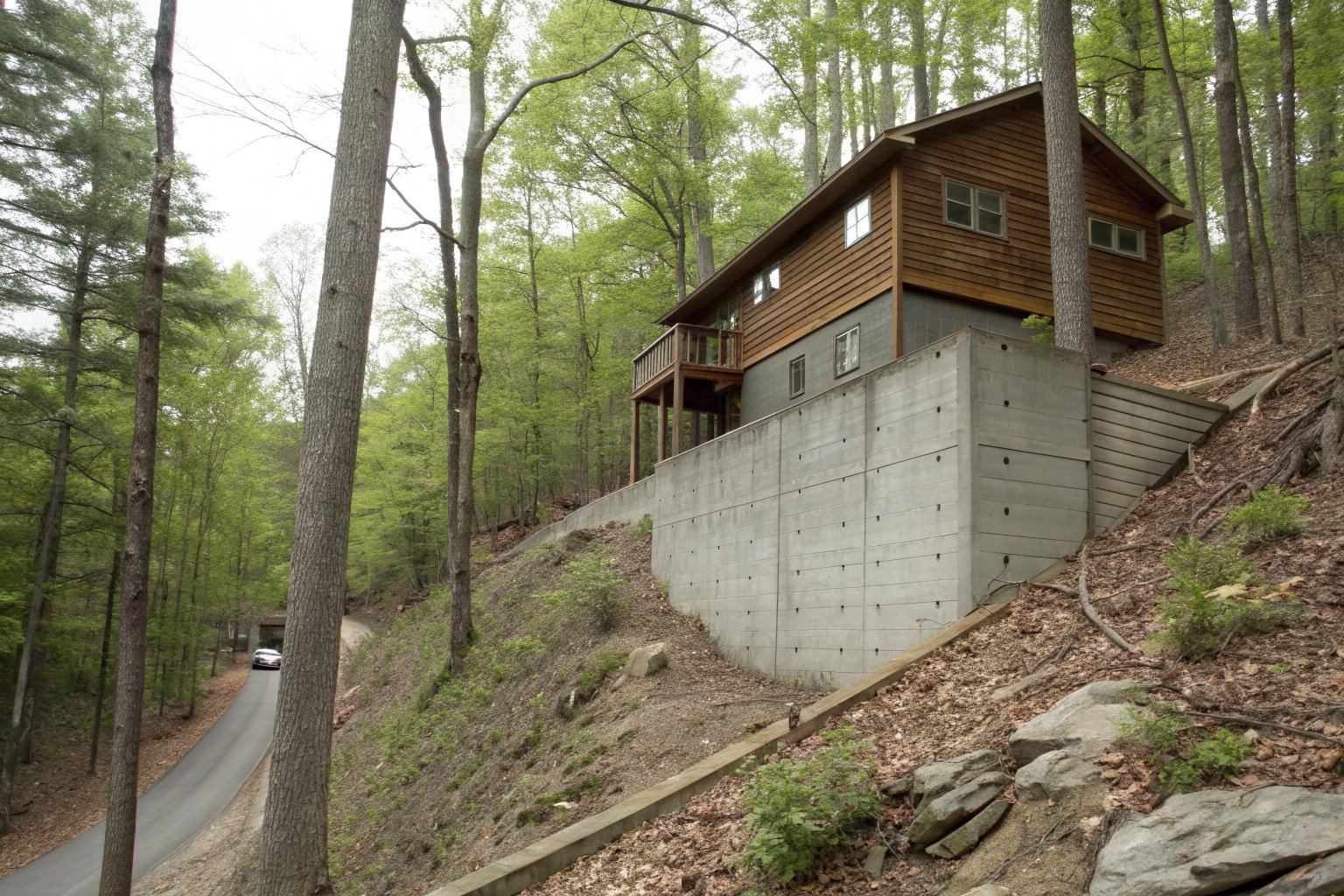 Two-story wood-sided house on a steep wooded lot, seen from below with its tall foundation wall